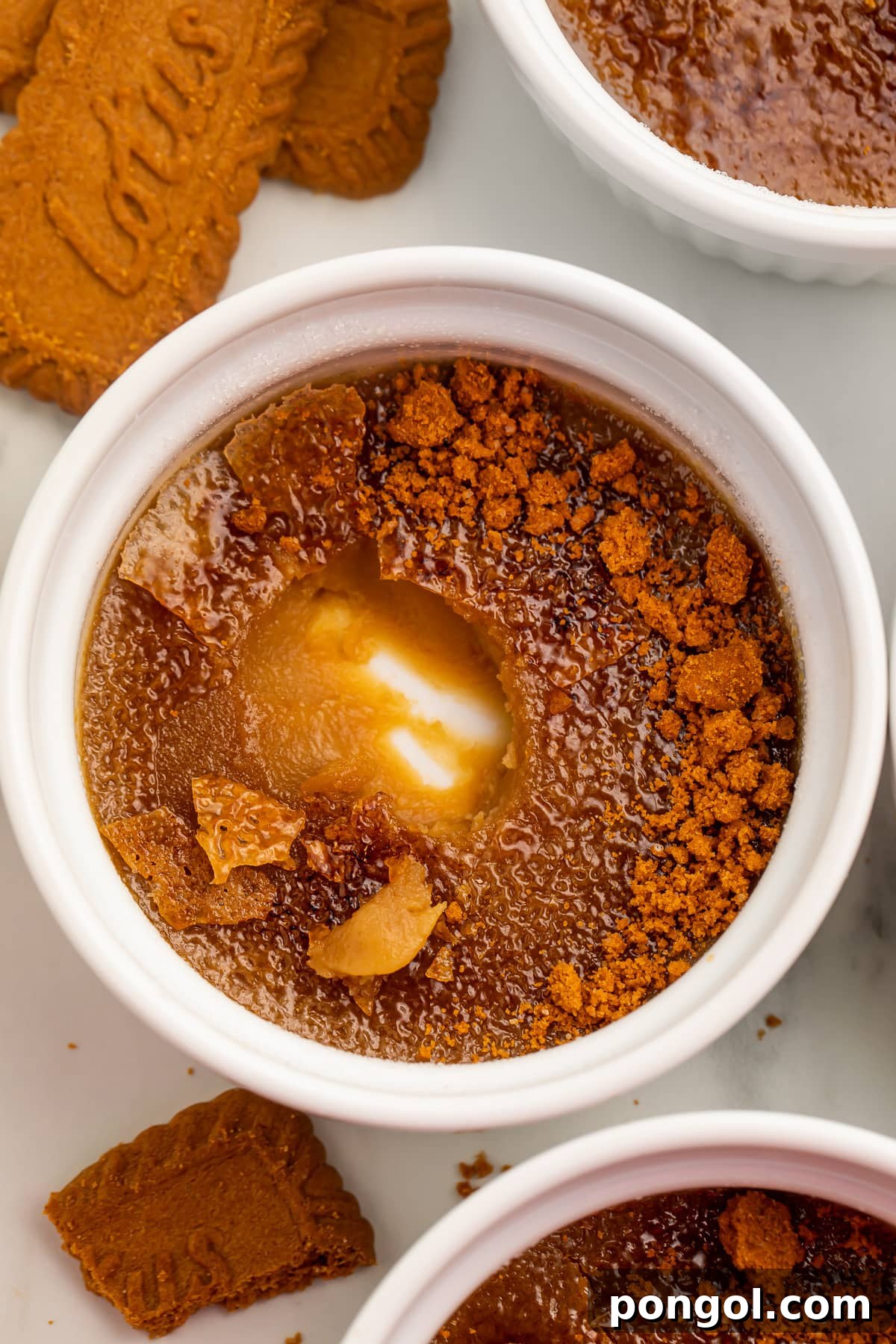 Biscoff cookie butter creme brulee in a round white ramekin with one spoonful missing from the center, showing the bottom of the ramekin.