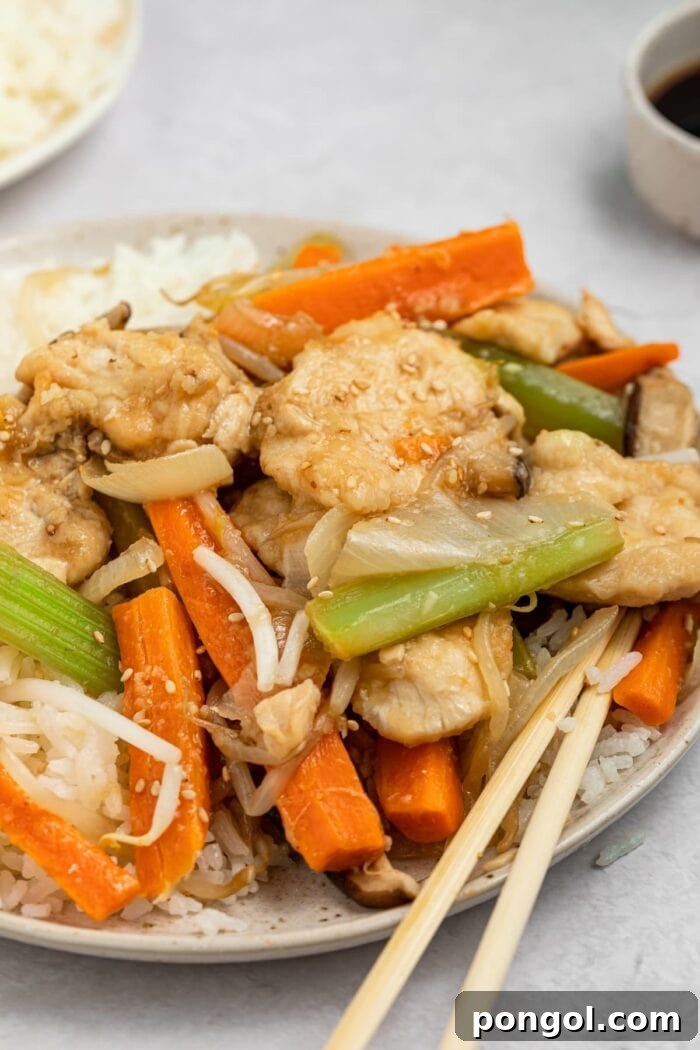 A close-up of chicken chop suey served on a white plate with chopsticks and a side of steamed rice.