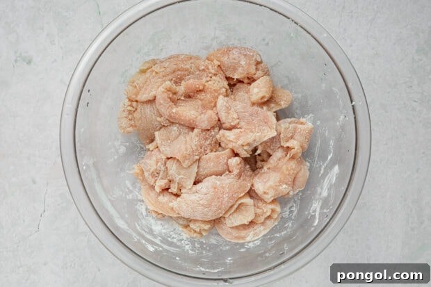 Thinly sliced chicken breast coated with cornstarch and salt in a bowl.