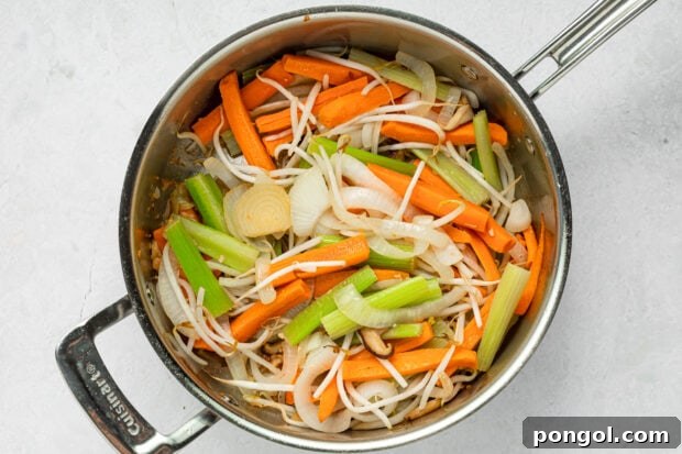 Mixed vegetables (mushrooms, onion, celery, carrots, garlic) stir-frying in a skillet.