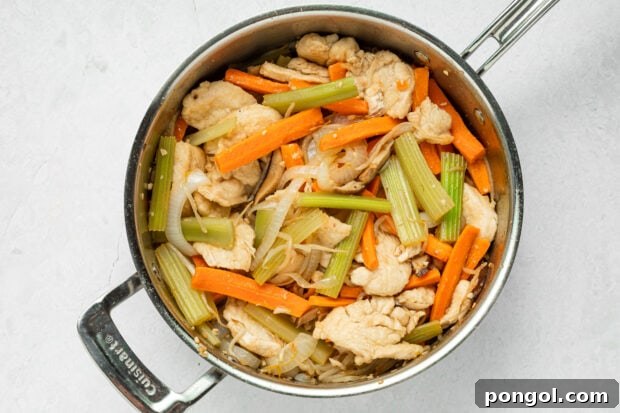 Cooked chicken and stir-fried vegetables simmering in the sauce in a skillet.