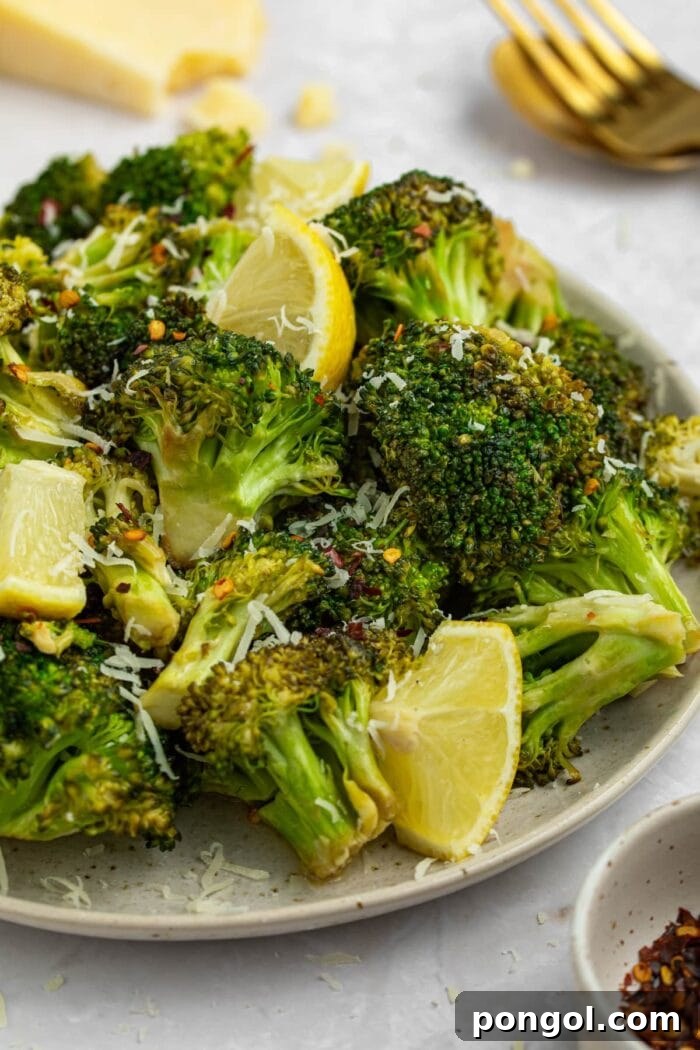 grilled broccoli on a plate with lemon slices and parmesan cheese on the side