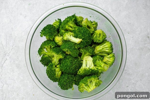 Broccoli florets being tossed with olive oil, lemon juice, and salt in a bowl.