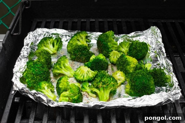 Grilled broccoli on aluminum foil on a grill grate, showing light charring.