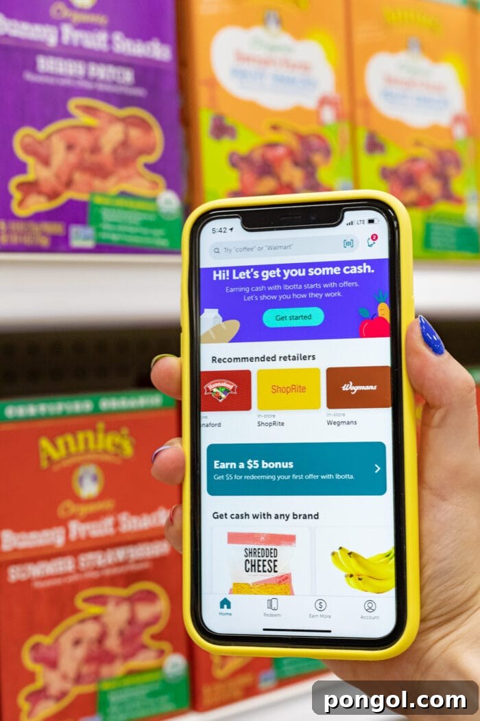 Ibotta app on iPhone in yellow case in front of a row of healthy snacks in a grocery store, showing cash back offers