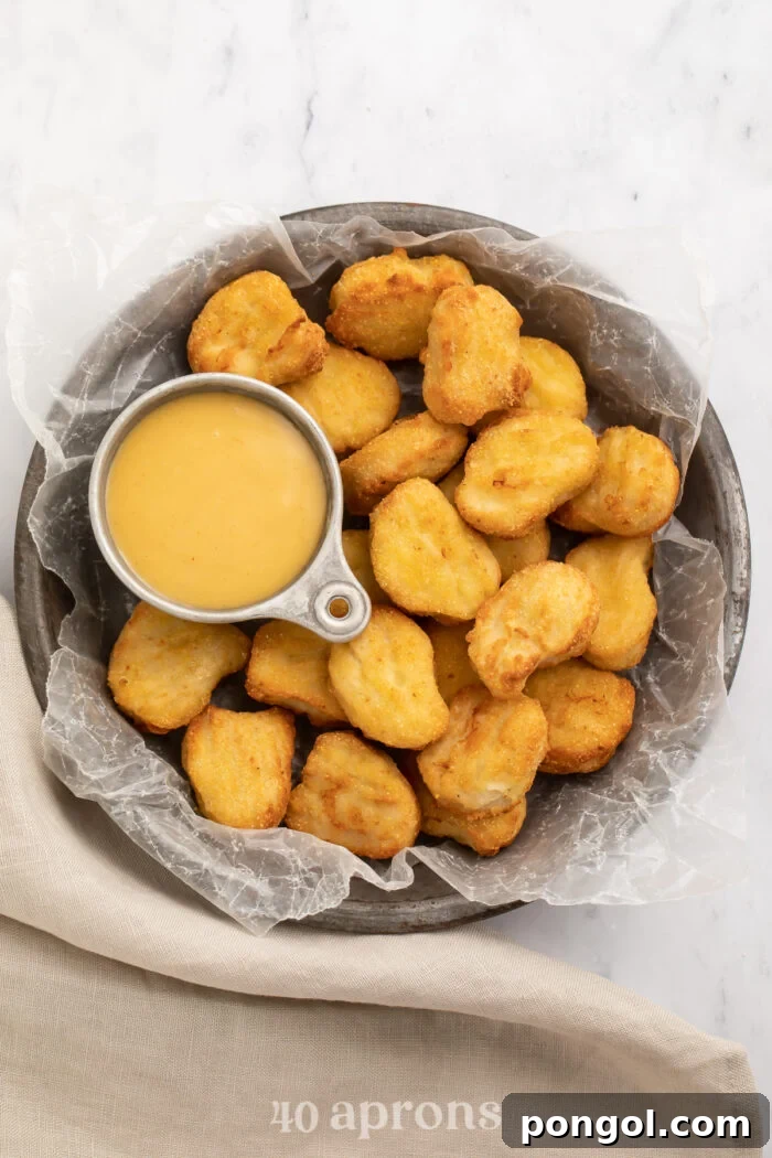 Overhead view of a large bowl of air fryer frozen chicken nuggets with a small dipping bowl of honey mustard.