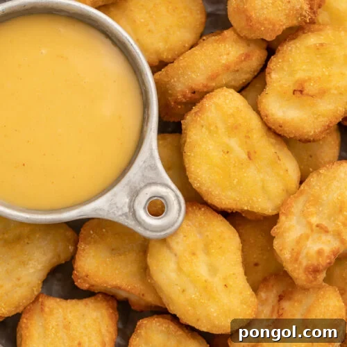Close-up of air fryer frozen chicken nuggets in a large bowl, next to a small dipping bowl filled with honey mustard sauce.
