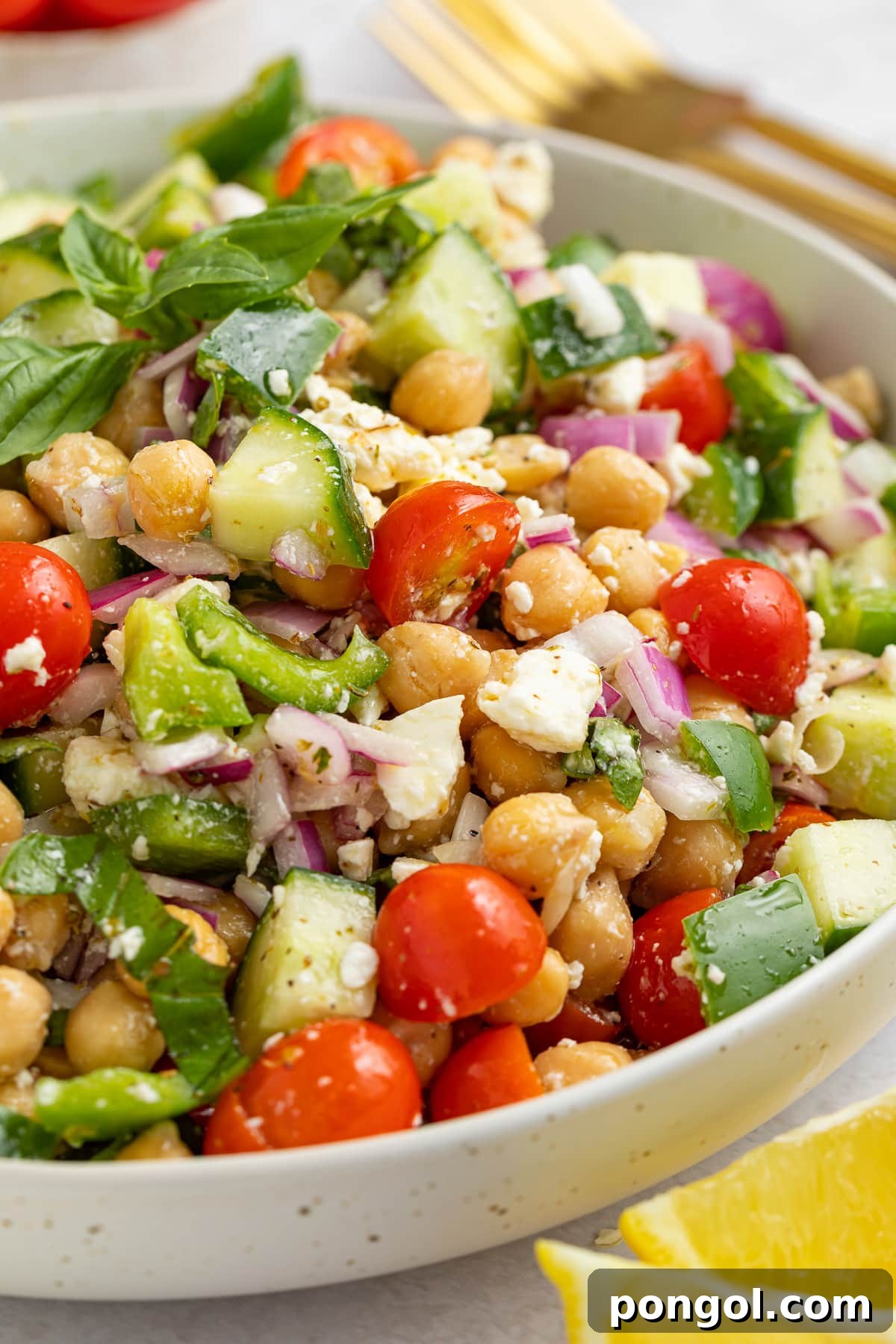 A large white bowl holding a Mediterranean-style chickpea salad with feta, bright red cherry tomatoes, chickpeas, cucumber, onion, and bell pepper.