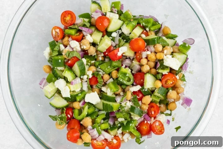Ingredients for Mediterranean chickpea salad in a large glass mixing bowl, before dressing is added.