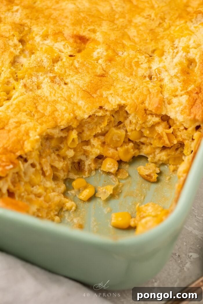 Angled photo of a golden-brown corn souffle with a scoop missing from the corner, revealing its fluffy, creamy interior.