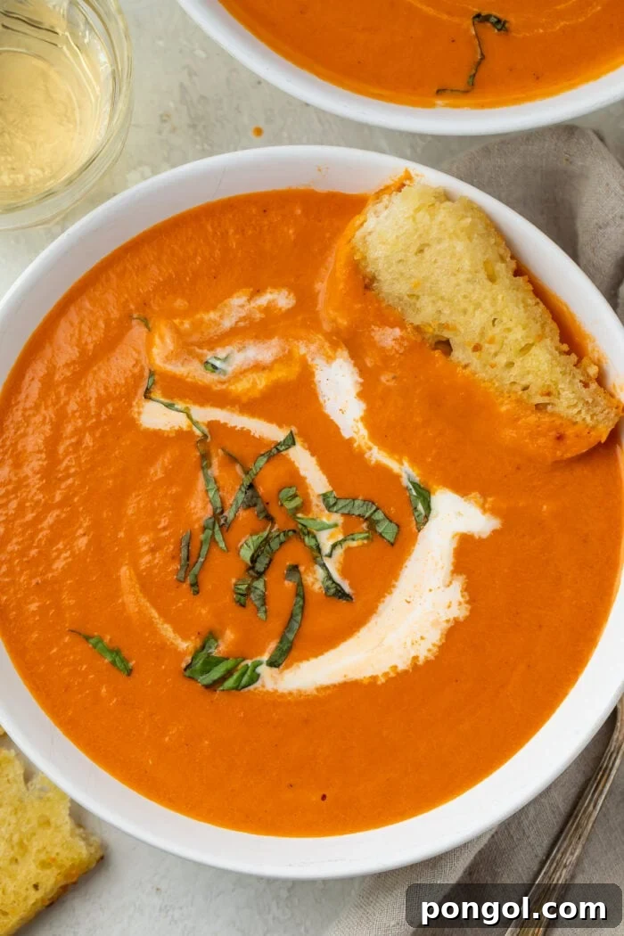 Closeup photo of tomato bisque in a white bowl with a swirl of cream and piece of bread