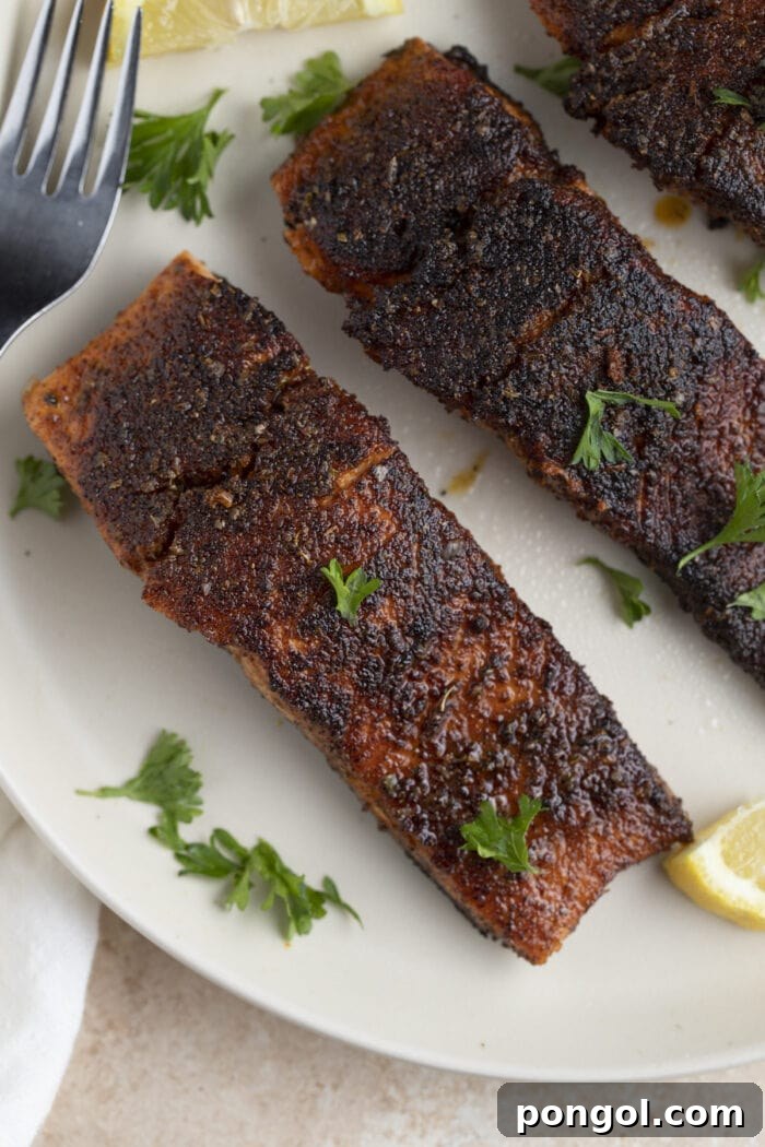 3 blackened salmon filets on a white plate with a lemon wedge