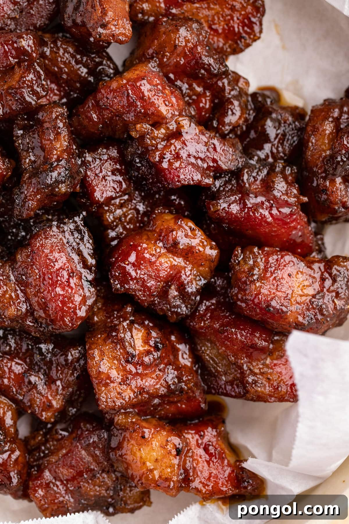 Crispy Grilled Pork Belly Bites 2 Perfectly cooked pork belly burnt ends resting on white parchment paper, showcasing their deep, caramelized exterior.