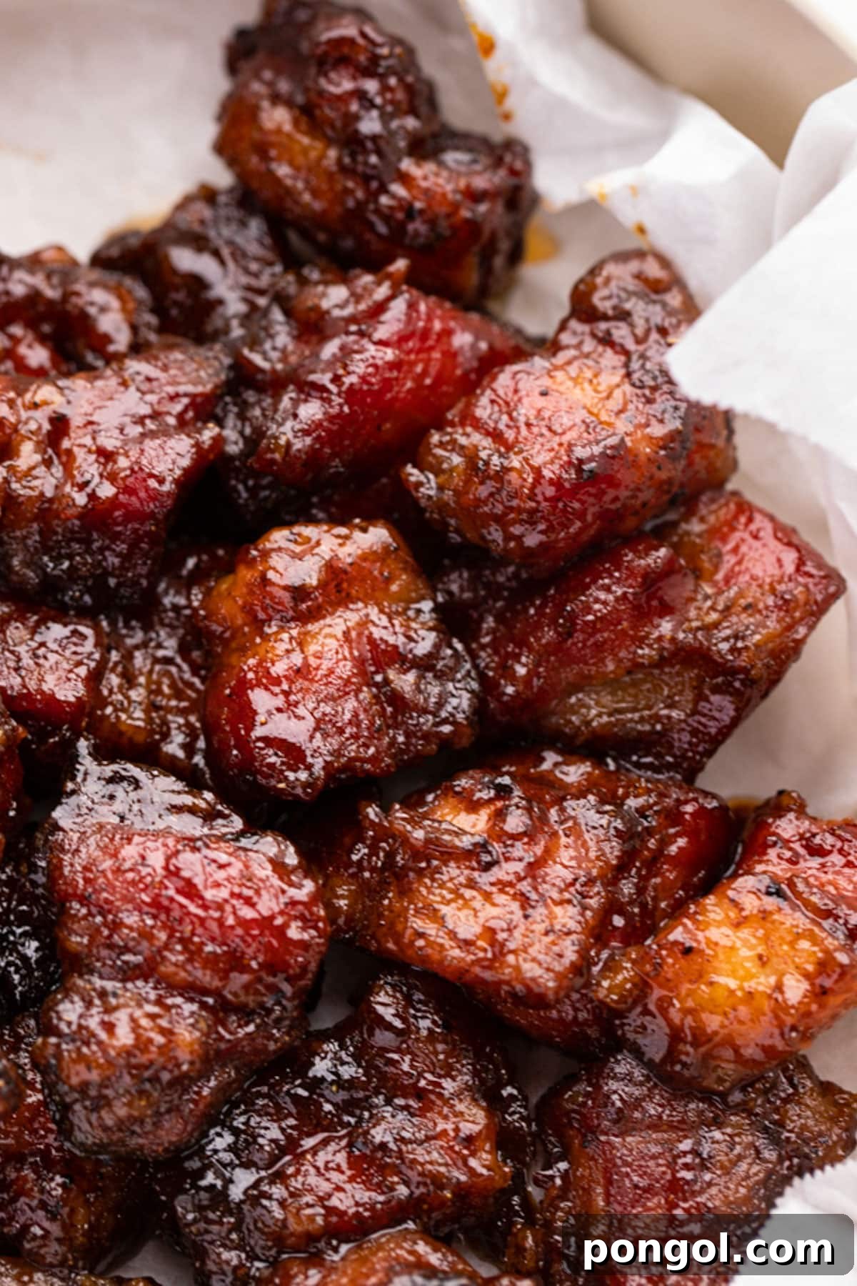 Crispy Grilled Pork Belly Bites 3 Close-up of freshly grilled pork belly burnt ends, glistening with BBQ sauce on white parchment paper.