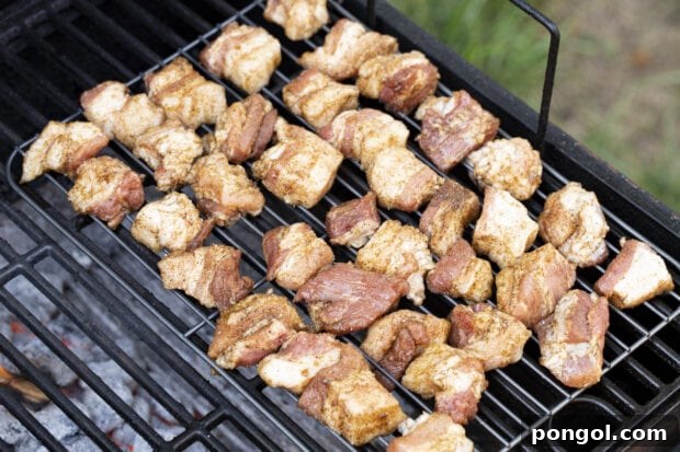 Crispy Grilled Pork Belly Bites 9 Pork belly cubes smoking on a charcoal grill over indirect heat.