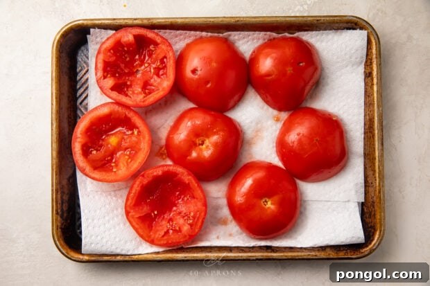 Halved tomatoes draining on a baking sheet lined with paper towels