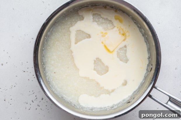 Creamy Cheese Grits Perfection: Stone-Ground and Quick Methods 12 Overhead view of grits, water, butter, and heavy cream in a large silver saucepan.