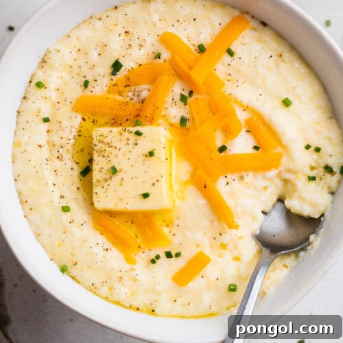 Creamy Cheese Grits Perfection: Stone-Ground and Quick Methods 4 Overhead view of a white bowl of grits topped with shredded cheese, a pat of butter, and black pepper.