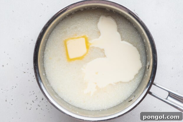 Creamy Cheese Grits Perfection: Stone-Ground and Quick Methods 8 Overhead view of grits, water, butter, and heavy cream in a large silver saucepan.