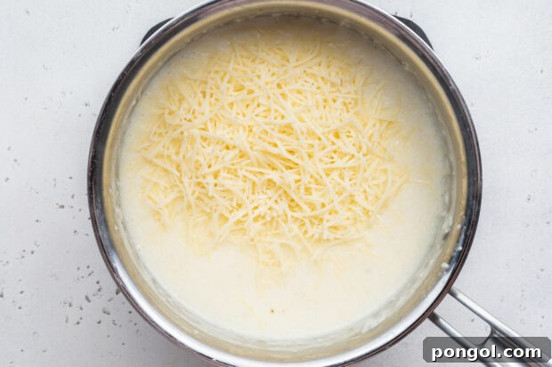 Creamy Cheese Grits Perfection: Stone-Ground and Quick Methods 9 Overhead view of grits and cream in a heavy saucepan with fresh shredded cheese.