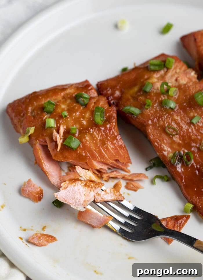 Perfect Miso Glazed Salmon 3 Close-up of miso salmon fillets on a white plate, with one fillet cut open by a fork to reveal its perfectly flaky, tender interior.
