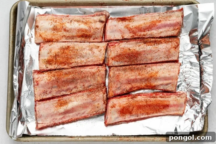 Tender beef back ribs on a baking sheet after slow cooking, ready for the final barbecue sauce application.