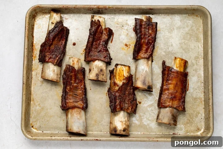 Caramelized BBQ beef back ribs on a baking sheet, showing a glossy, slightly charred finish after broiling.