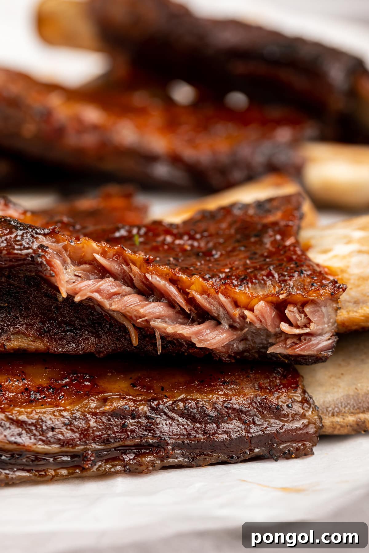 Close-up side view of perfectly cooked BBQ beef back ribs, showing the tender, juicy meat pulling effortlessly away from the bone, highlighting its succulent texture.