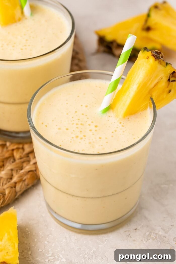 Tropical Pineapple Bliss 2 Two short glasses of golden pineapple smoothie, garnished with fresh pineapple wedges, ready to be enjoyed.