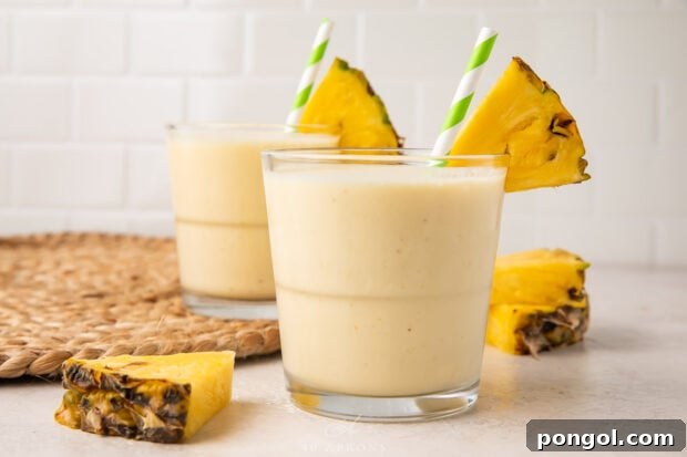 Tropical Pineapple Bliss 7 Side view of 2 glasses of pineapple smoothie with pineapple wedges, ready to be served.