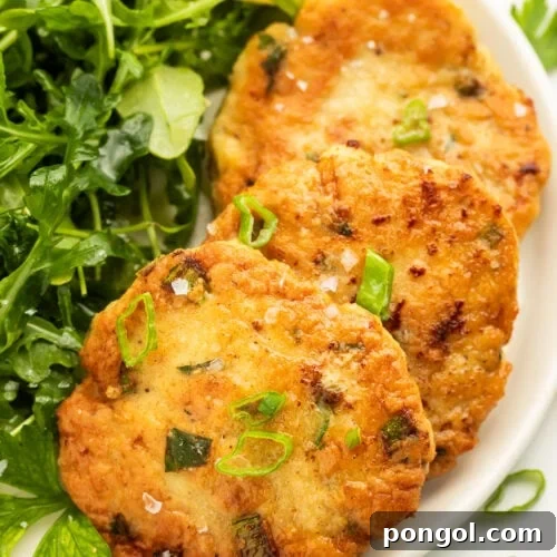 Perfectly Crispy Chicken Patties Close-up of three golden pan-fried chicken patties on a white plate with a sprig of fresh parsley, emphasizing their crispy texture.