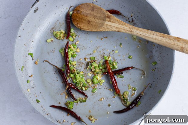 Aromatics for kung pao beef in large skillet with wooden spoon