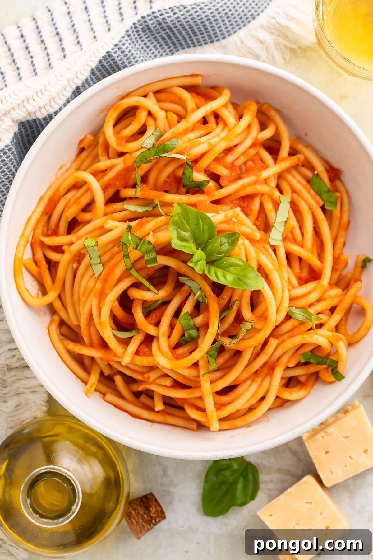 Classic Pomodoro Perfection 2 Overhead view of a white bowl of spaghetti swirled with red pomodoro sauce and topped with fresh basil leaves.