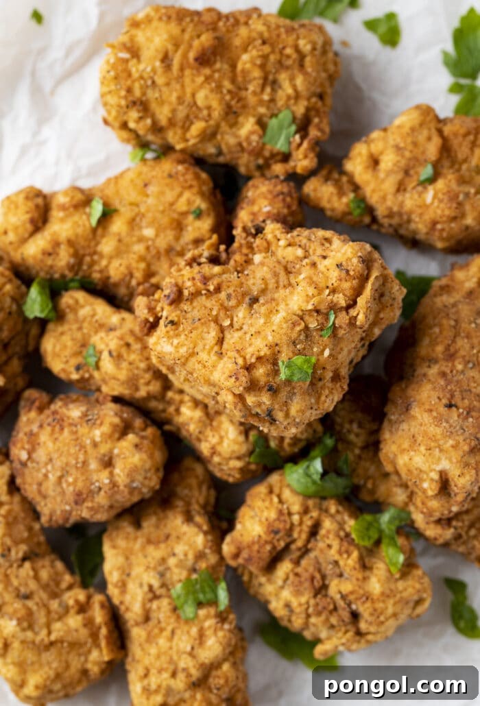 Vegan Fried Tofu Chik'n 3 Two pieces of golden crispy vegan fried chicken on a white plate with a side of greens.