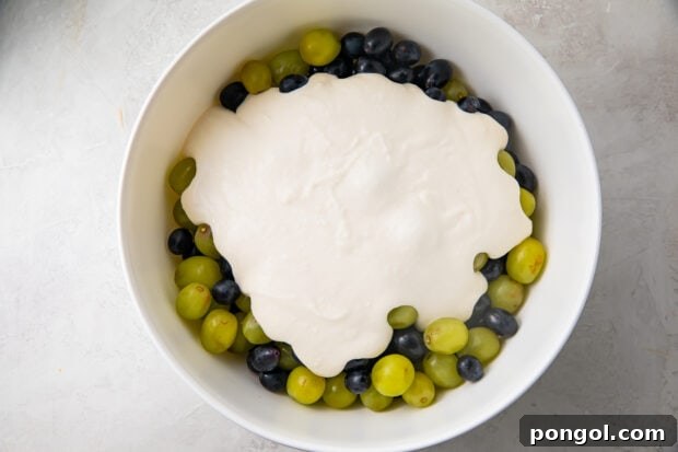 Sweet dressing mixture added to bowl of red and green grapes, ready to mix