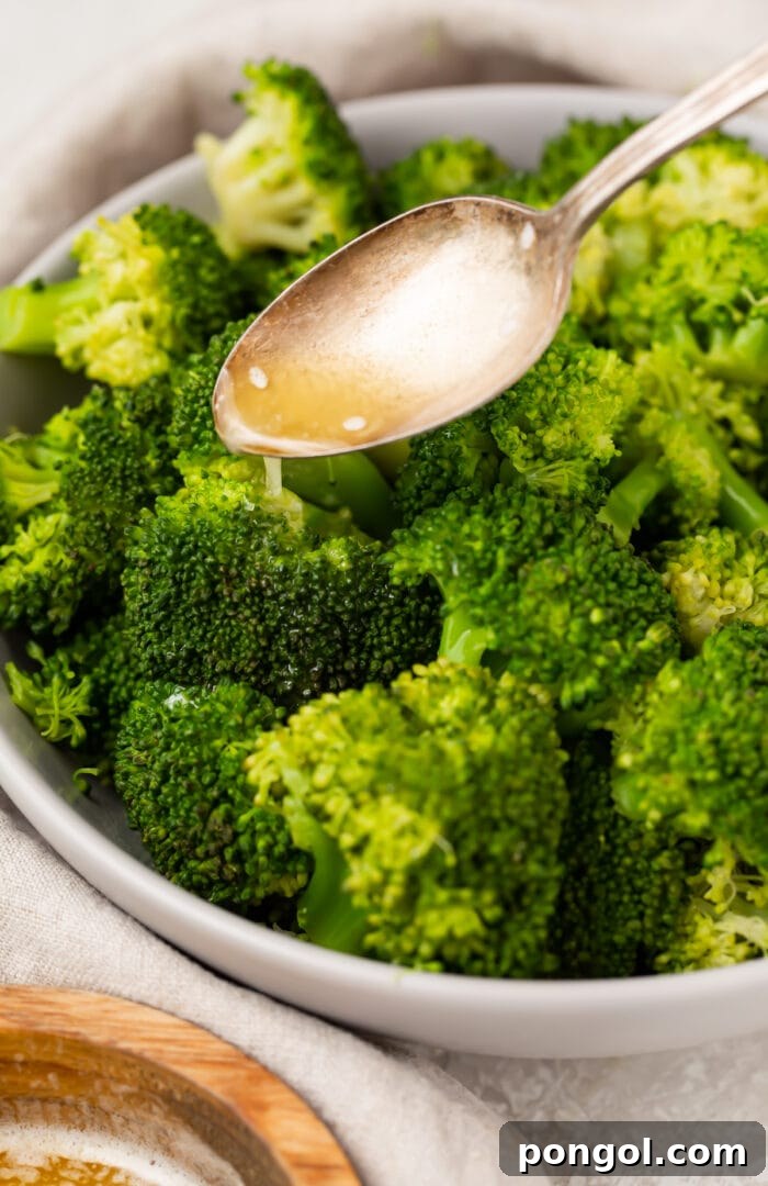 A spoon drizzles lemon butter sauce over Instant Pot broccoli in a large white bowl