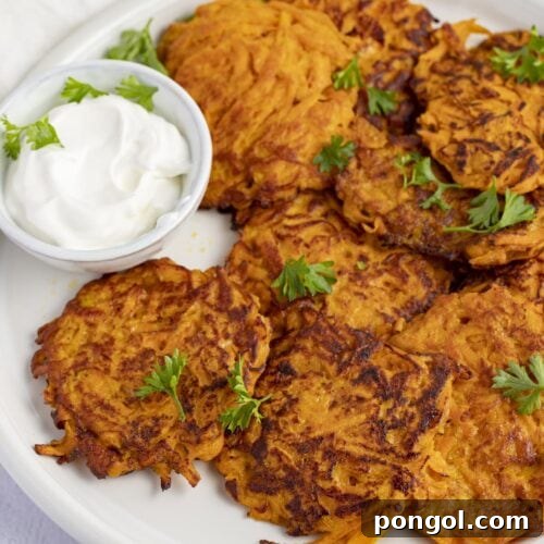 Sweet potato hash browns on a white plate next to sour cream, showcasing the crisp exterior