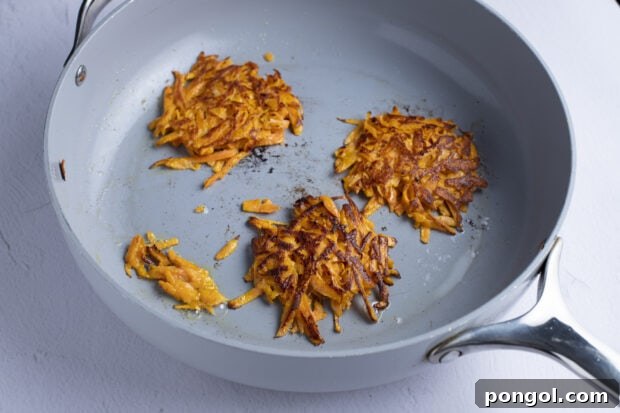 Sweet potato hash browns frying in a large skillet, turning golden brown