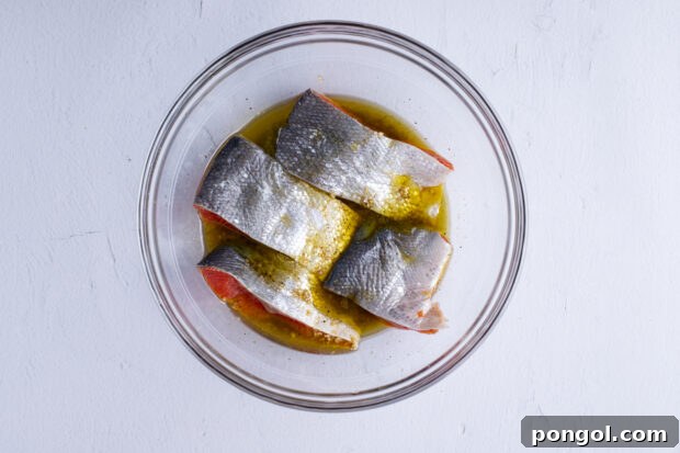 Salmon fillets soaking in the marinade in a bowl, covered with plastic wrap.
