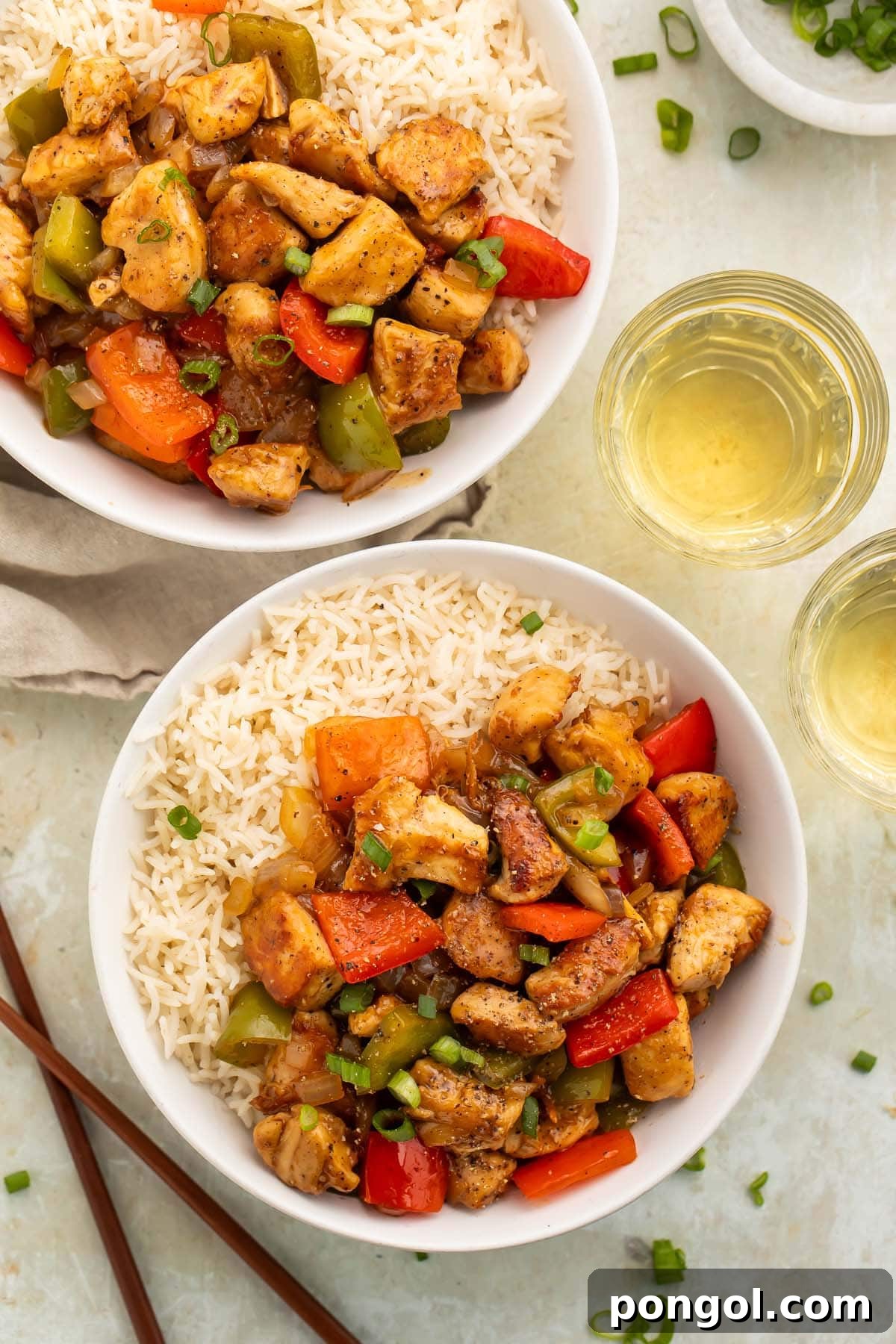 Overhead photo of a bowl of white rice topped with black pepper chicken and vegetables on a table. Delicious and easy Black Pepper Chicken, garnished with fresh herbs.