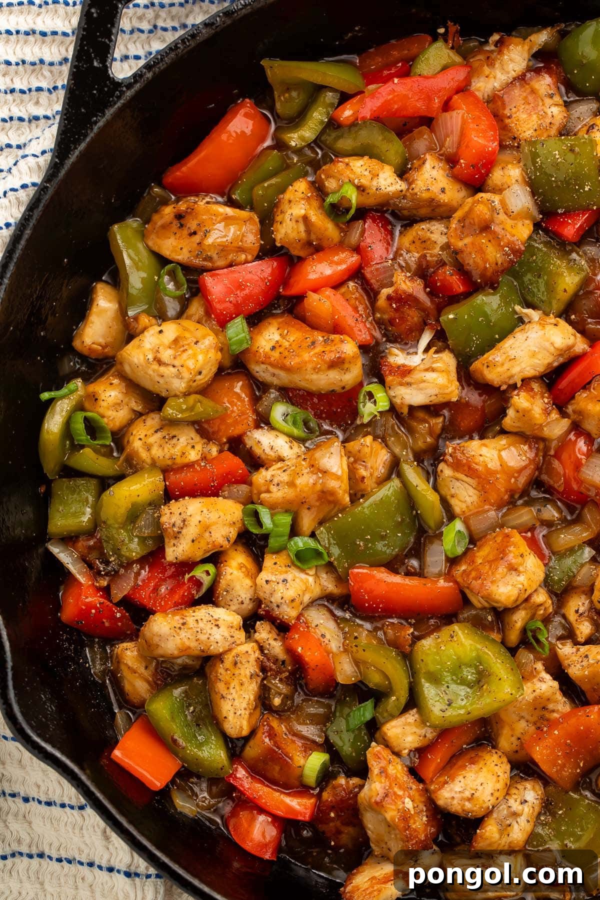 A large cast-iron skillet filled with sizzling black pepper chicken and colorful vegetables, fresh off the stove.