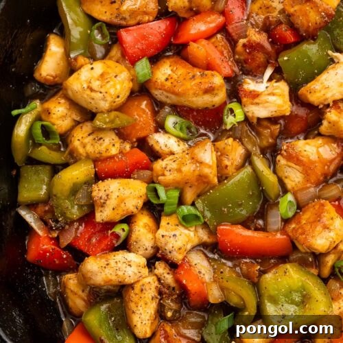 A large cast-iron skillet holding black pepper chicken and vegetables, ready to be served.