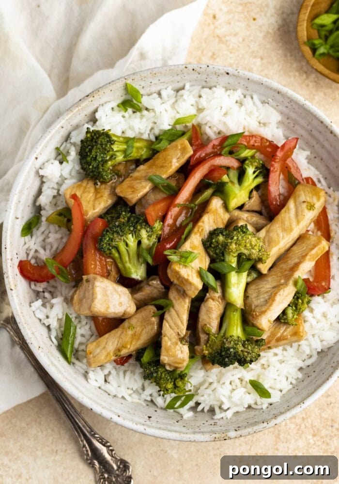 Flavorful Pork Stir Fry served over a bed of fluffy white rice in a pristine white bowl, accompanied by a neatly folded napkin and a spoon, ready to be enjoyed.