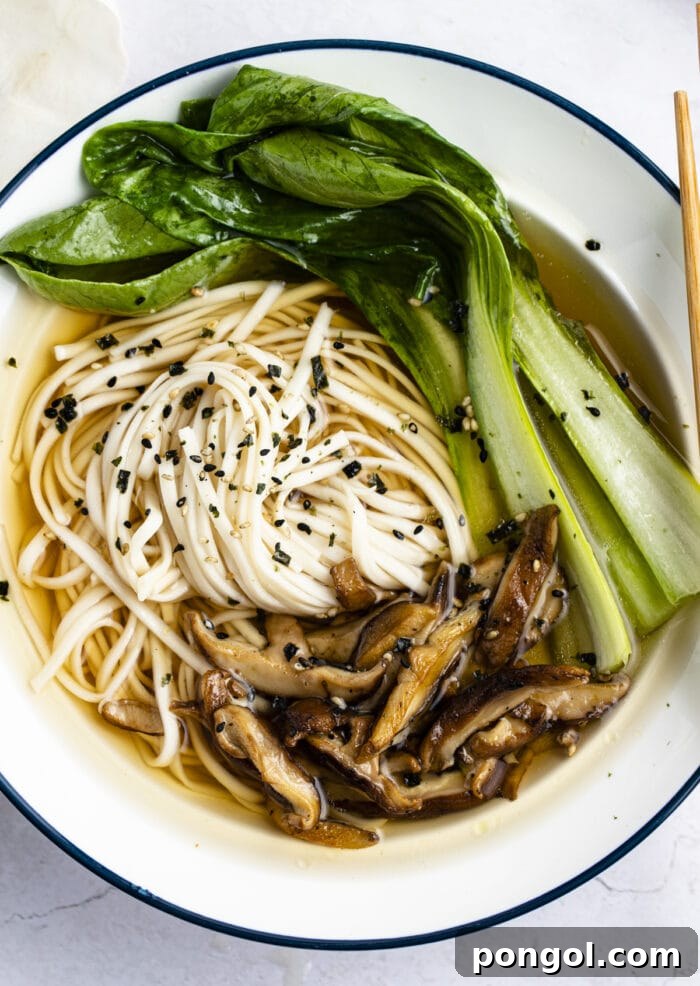 Close-up of tender Udon noodles in a savory broth, garnished with fresh green onions and other toppings, in a blue-trimmed bowl.