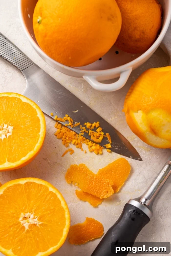 Fresh oranges, orange zest, and a knife on a cutting board