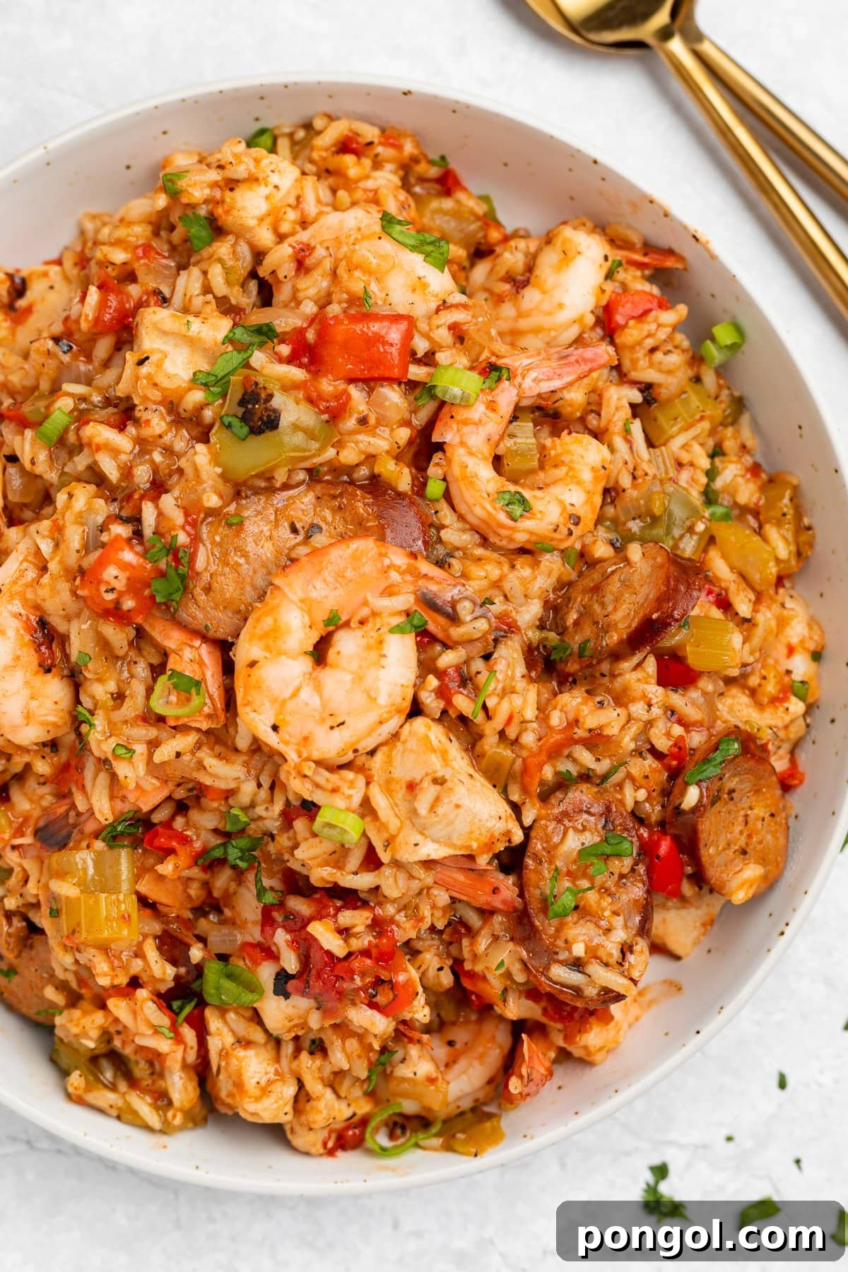 Overhead photo of a large white bowl holding Instant Pot jambalaya with rice, shrimp, sausage, and veggies, garnished with fresh herbs.
