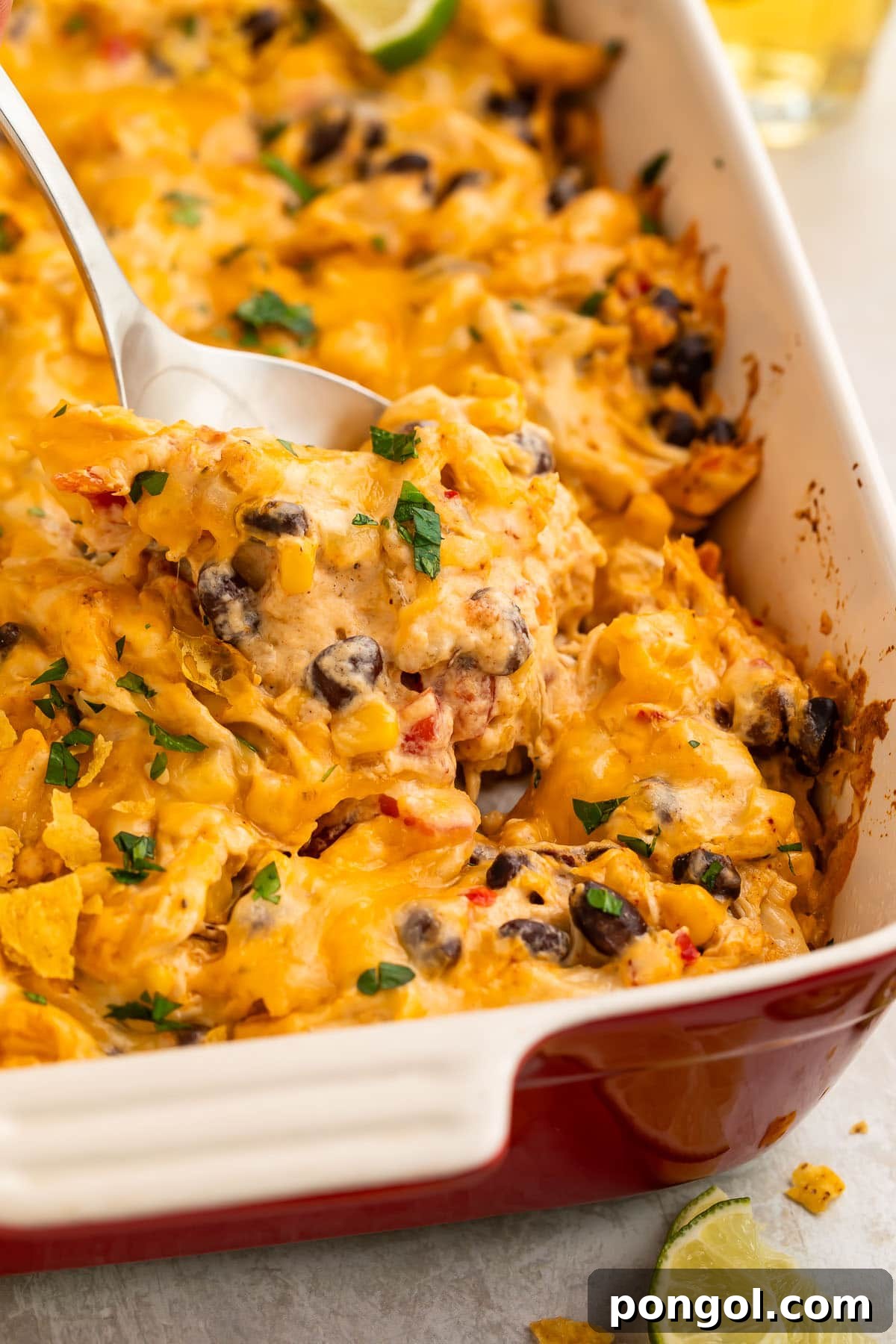 A spoonful of Mexican chicken casserole being lifted out of a large casserole dish, showcasing its rich layers and melted cheese.