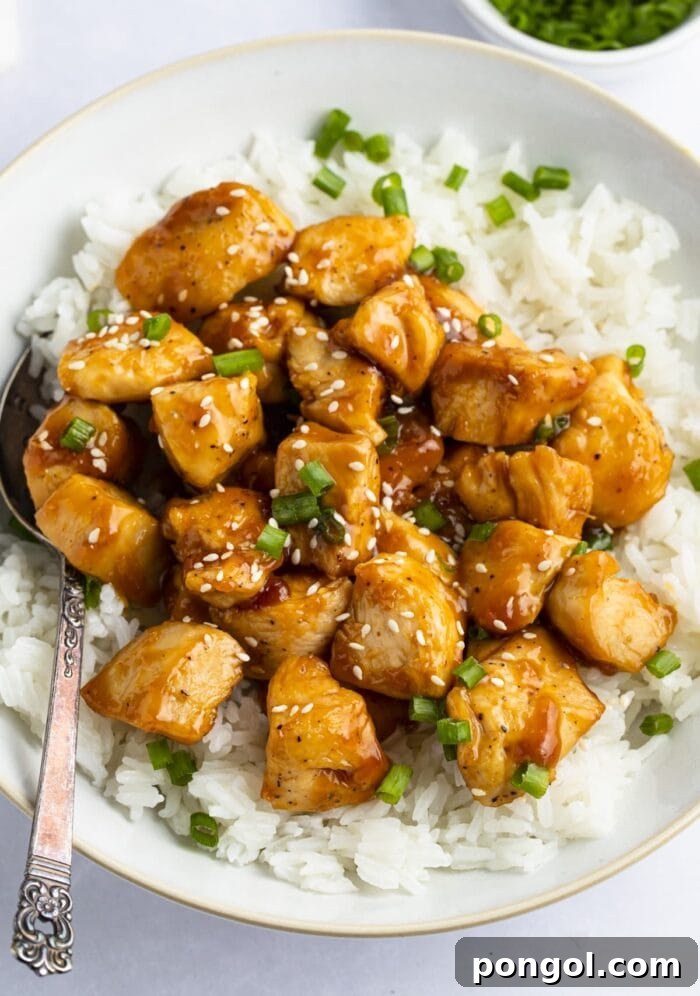 Mandarin chicken with rice in large bowl - A close-up shot of a vibrant, glistening mandarin chicken dish served over fluffy white rice in a large bowl, garnished with fresh green onions and sesame seeds.