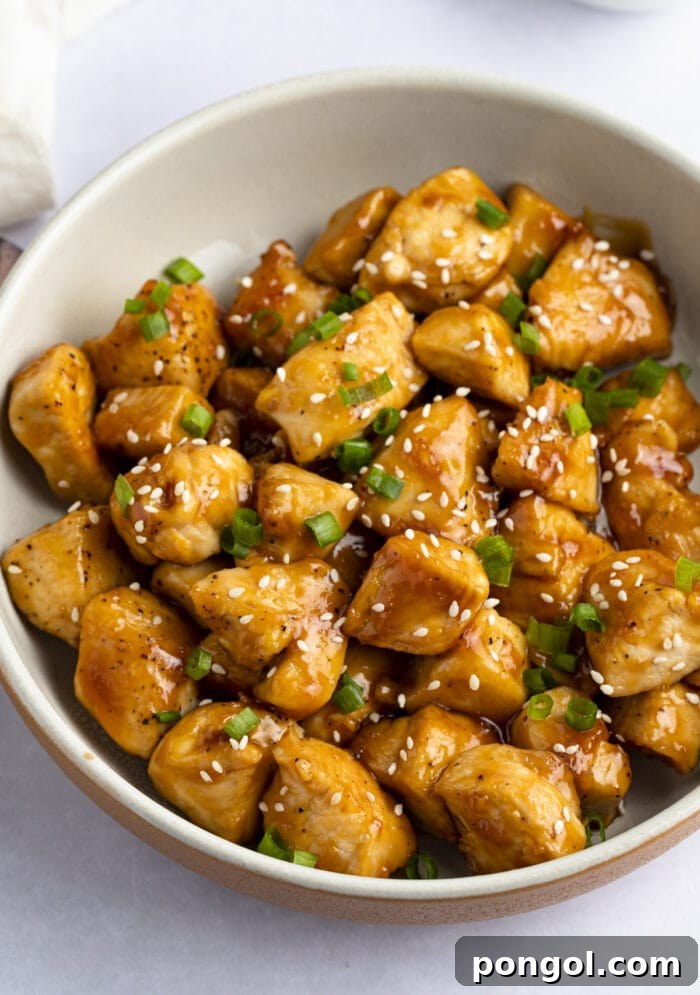 Mandarin chicken in large bowl - A close-up, top-down view of a large serving bowl filled with glazed mandarin chicken, garnished with fresh green onions and sesame seeds, ready to be served.