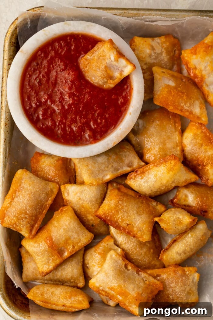 A close-up shot of crispy air-fried pizza rolls piled on a plate, with a small bowl of pizza sauce in the background, ready for dipping.